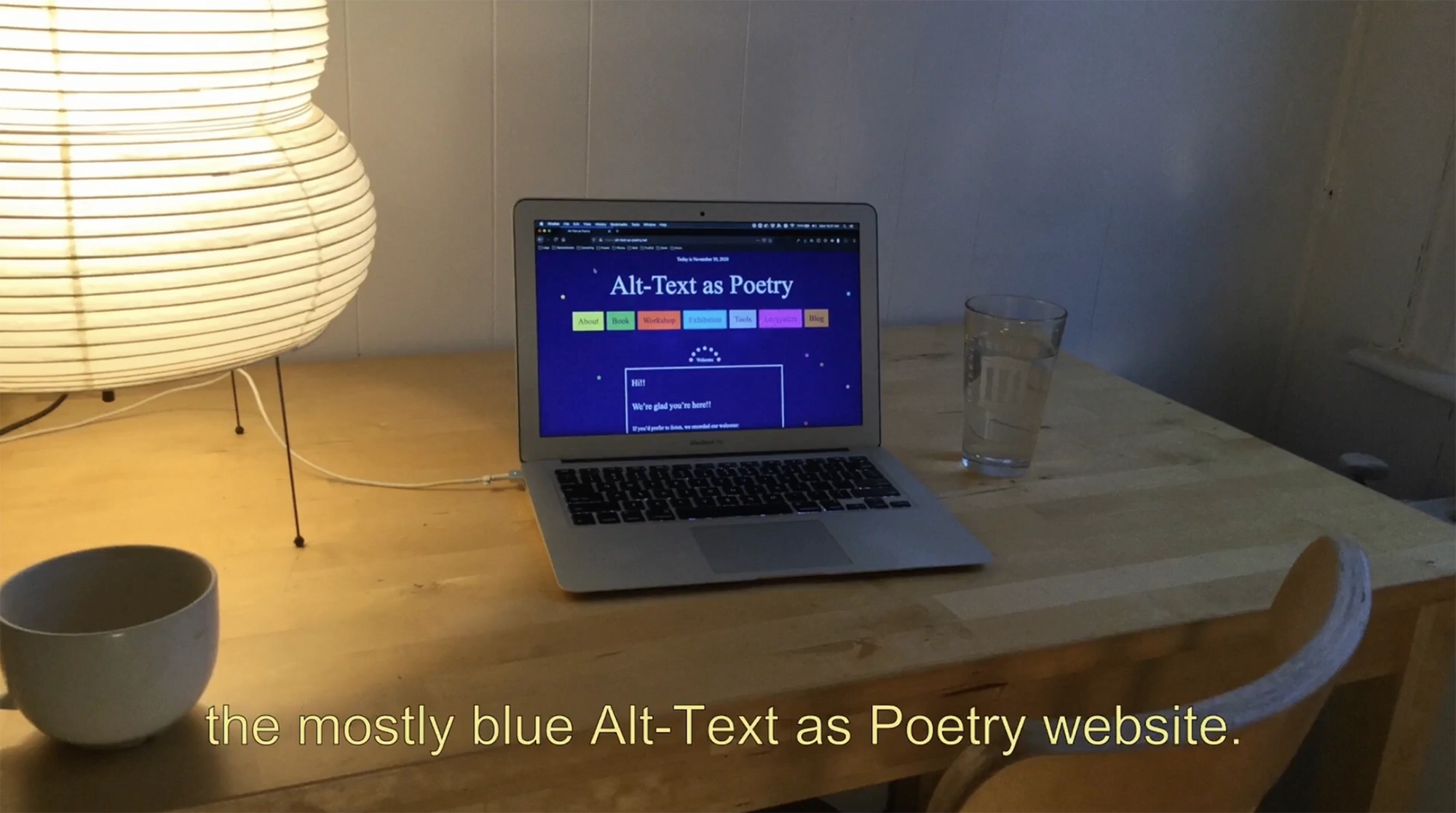 a photo of a laptop on a light wooden desk with the mostly blue Alt Text as Poetry website displayed on it