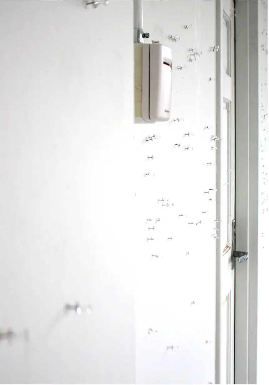 photograph of a empty white wall taken from the side, showing many thumbtacks