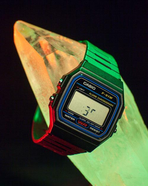 a photograph of a black casio watch placed on a crystal, lit with green and red light against a black background. it shows a faded :35 on its digital display