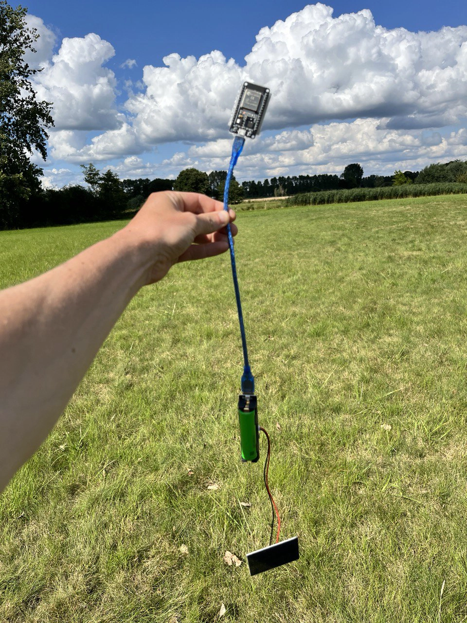photo of Ben Earl holding a small server with a solar panel attached for the coding in situ workshop with a grass field behind